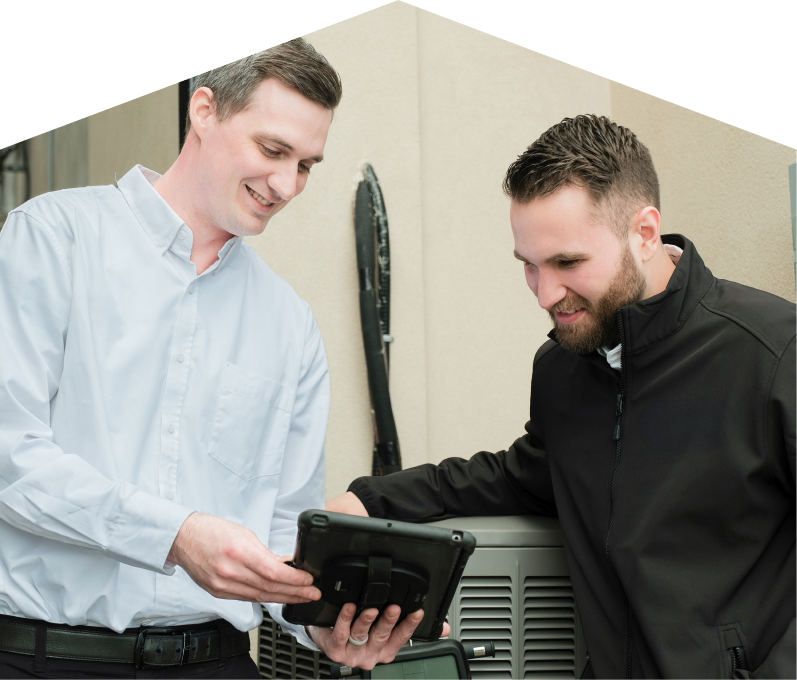 A Dunn technician in a white shirt shows service details on a tablet to a smiling client in a black jacket, standing beside an AC unit outside a beige building.
