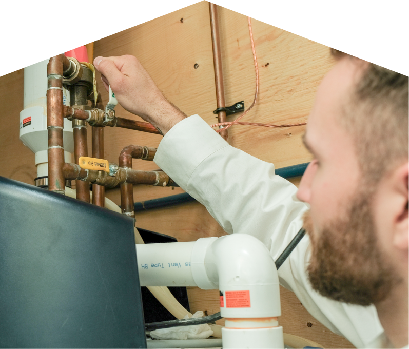 Dunn water heater specialist tightens a valve on copper piping during a water heater installation, with exposed wood paneling and wiring in the background. Dunn water heater specialist tightens a valve on copper piping during a water heater installation, with exposed wood paneling and wiring in the background.